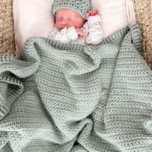 Puede incluir: Una manta de beb&eacute; tejida a ganchillo en color verde salvia con un patr&oacute;n de punto de estrella texturizado, acompa&ntilde;ada de un gorro de beb&eacute; a juego en ganchillo verde salvia con dos peque&ntilde;as orejas redondeadas en la parte superior.