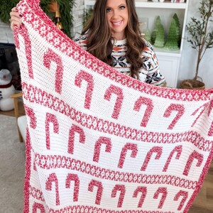 K&ouml;nnte beinhalten: Eine wei&szlig;-rote H&auml;keldecke mit einem Zuckerstangenmuster. Die Decke hat einen roten Rand und Zuckerstangenmuster. Die Decke wird hochgehalten und zeigt das festliche Weihnachtsthema.