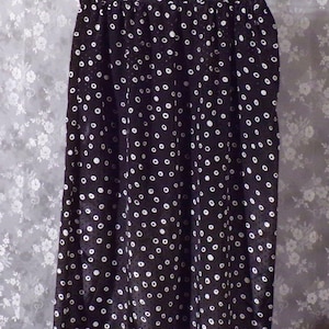 May include: A black skirt with a white polka dot pattern. The skirt is hanging on a hanger against a floral background. The skirt appears to be made of a lightweight fabric.