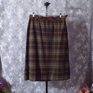 May include: A brown and green plaid skirt with a brown leather belt. The skirt is hanging on a hanger against a floral patterned background. The plaid pattern features shades of brown, green, and orange.