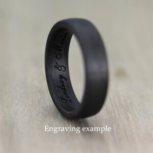 Op de afbeelding: Een zwarte carbonfiber ring met de inscriptie "Lindsay & Martin" gegraveerd aan de binnenkant van de band. Voorbeeld van een gravure.