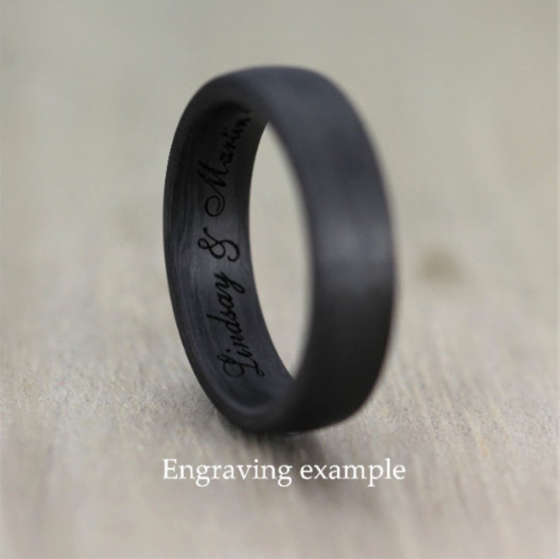 Op de afbeelding: Een zwarte carbonfiber ring met de inscriptie "Lindsay & Martin" gegraveerd aan de binnenkant van de band. Voorbeeld van een gravure.