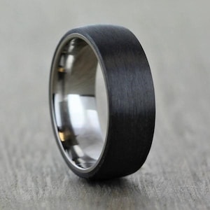 Op de afbeelding: Een zwarte en zilveren ring met een geborstelde afwerking. De ring is gemaakt van titanium en carbonfiber.