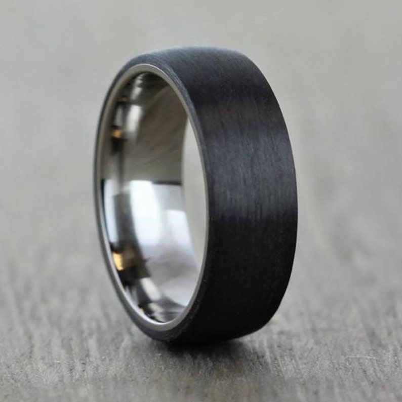 mans black wedding ring band, Polished titanium sleeve in comfort fit. Covered in Matte/brushed black Carbon Fibre. 6 millimetres wide 7mm Court shape and comfort fin. Th minimal dome shape of the ring sits with a low profile on the finger