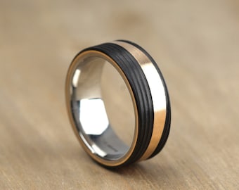 May include: A black and gold wedding band with a grooved texture. The band has a thin gold stripe around the edge.