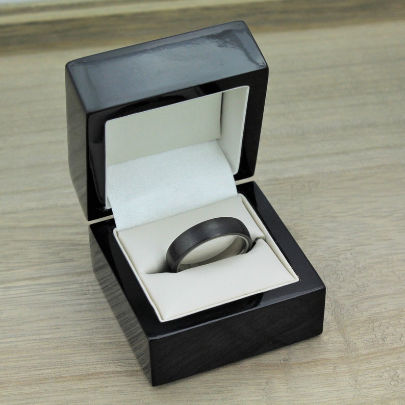 May include: A black ring box with a black ring inside. The box is made of wood and has a velvet lining.