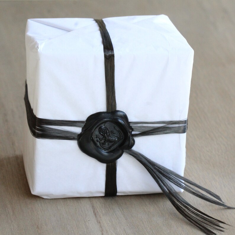 May include: A white gift box wrapped with black ribbon and a black wax seal. The seal has a design of a lion.