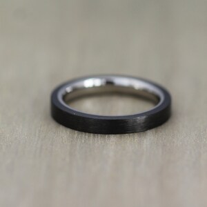 May include: A black and silver ring with a brushed finish. The ring is made of titanium and carbon fiber.