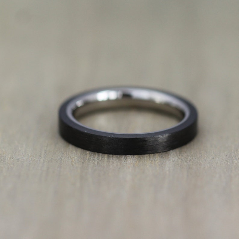 May include: A black and silver ring with a brushed finish. The ring is made of titanium and carbon fiber.