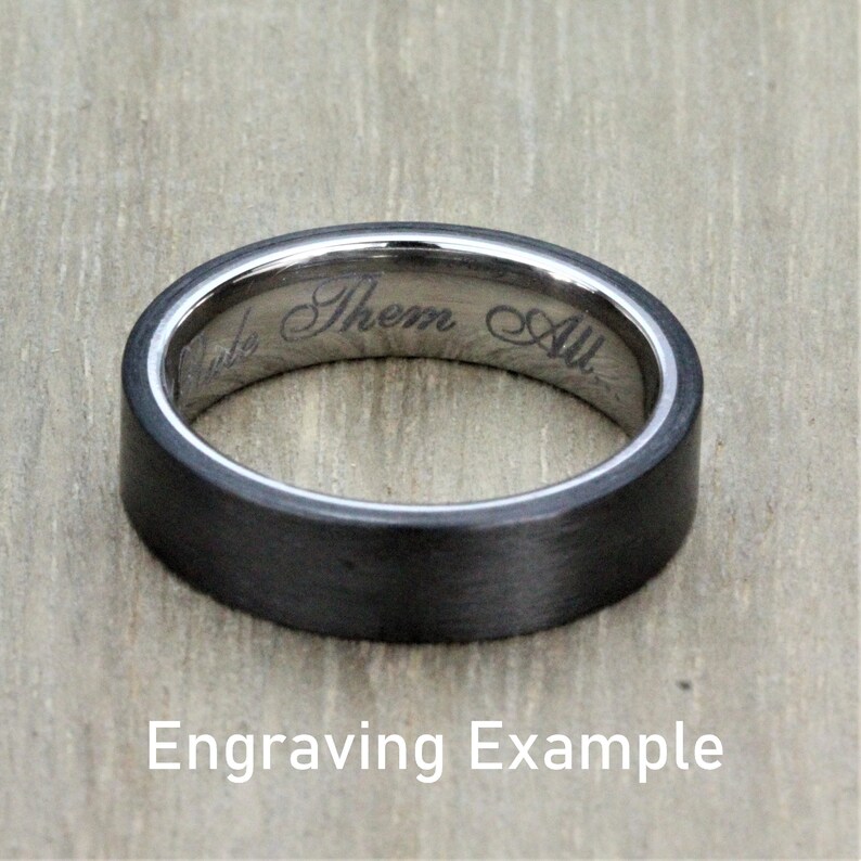 May include: A black and silver wedding band with an inscription that reads "Them All". Engraving example.