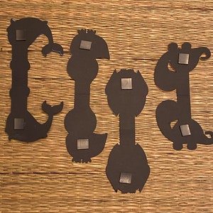 May include: Four black metal wall decor pieces in the shape of stylized animals. Each piece has a magnetic backing.