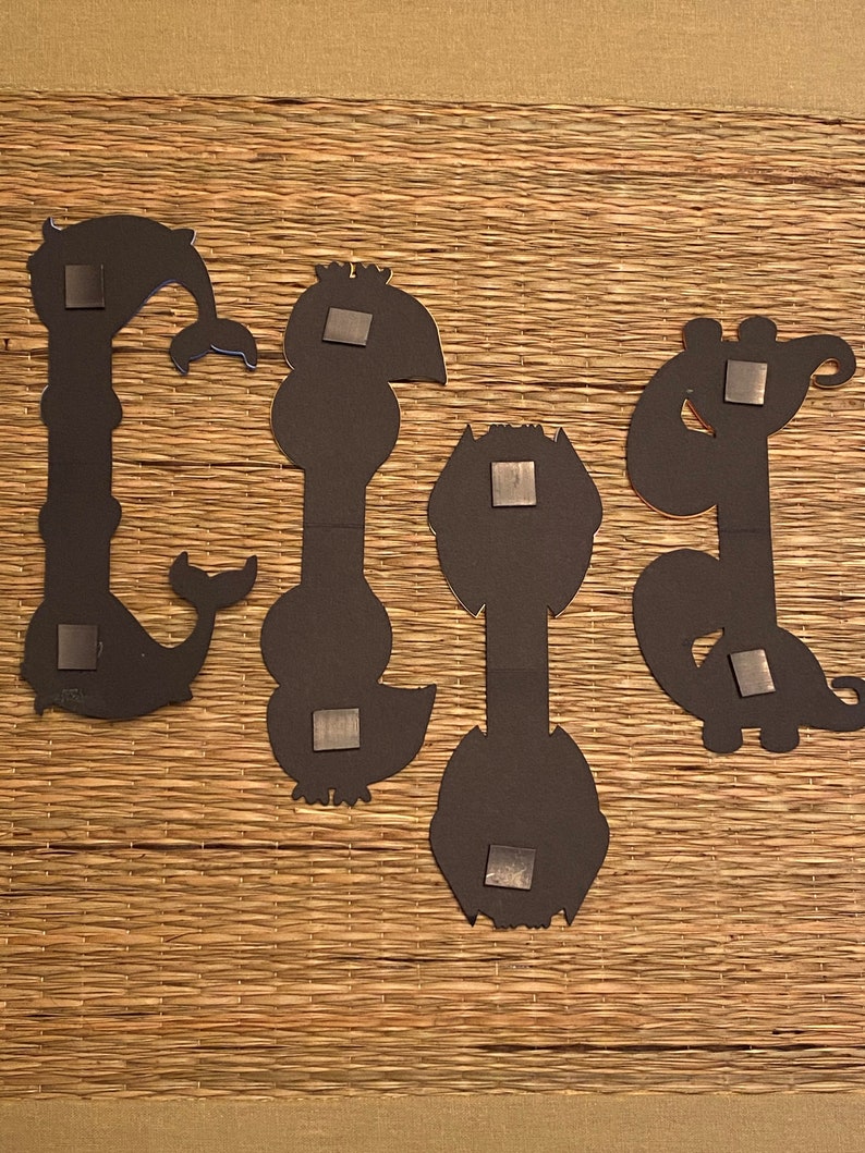 May include: Four black metal wall decor pieces in the shape of stylized animals. Each piece has a magnetic backing.