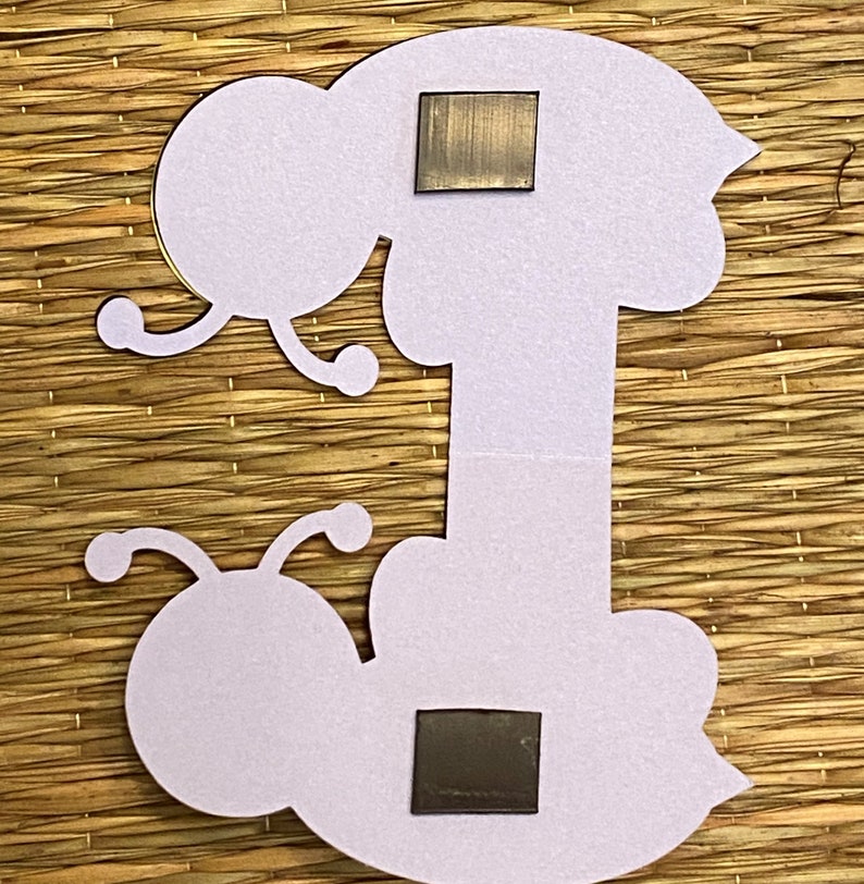 May include: A white felt craft cutout of a caterpillar with two black magnetic squares attached to the back.