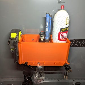 May include: An orange, wall-mounted tool organizer with various tools. Includes a tape measure, utility knife, Kobalt tools, a can of Gumout Performance, safety glasses, and keys. The organizer is mounted on a gray surface.