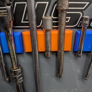 May include: A close-up of a tool organizer with various metal sockets and wrenches. The organizer has blue and orange holders. The background is gray with black and white text.