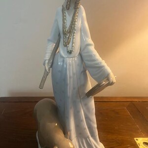 May include: A porcelain figurine of a woman in a blue and white dress with a brown bear at her feet. She is wearing a head scarf and multiple necklaces.