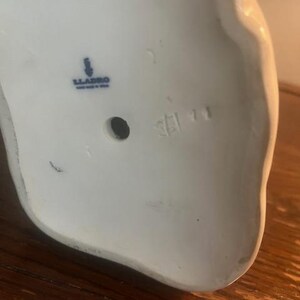 May include: The bottom of a white porcelain figurine with a blue Lladro logo and the number 5211.