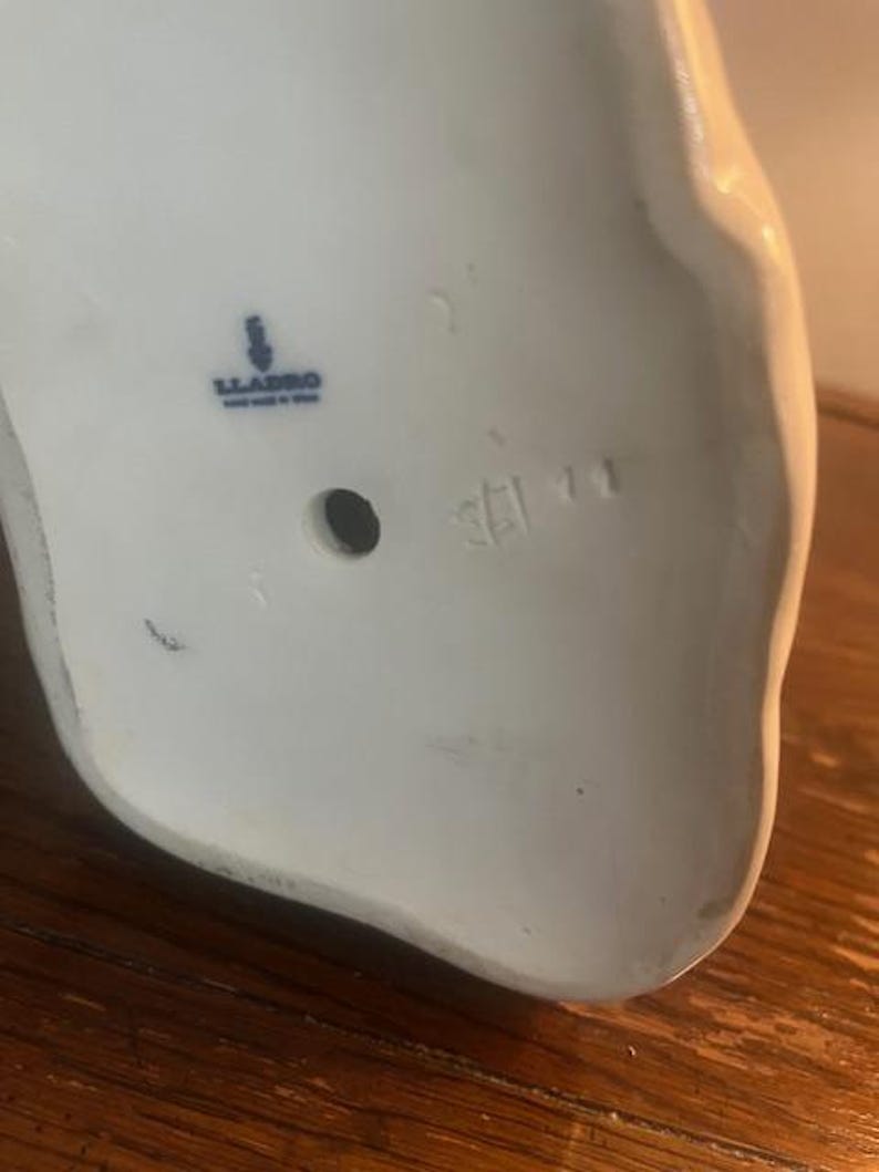 May include: The bottom of a white porcelain figurine with a blue Lladro logo and the number 5211.