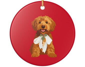 May include: A circular, red Christmas decoration with a cartoon illustration of a golden doodle dog wearing a white bow and holly. The ornament has a gold string for hanging.