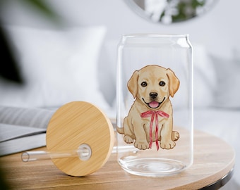 May include: A clear glass can-shaped tumbler featuring a smiling cartoon Labrador puppy with a red bow. The tumbler has a bamboo lid and a clear straw. The design is on a wooden table.