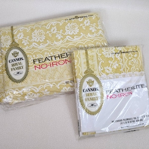 May include: Two packages of Cannon Royal Family bedding, one labeled "Feather No-Iron" and the other "Featherlite No-Iron". Both packages feature a yellow and white floral pattern with lace trim.