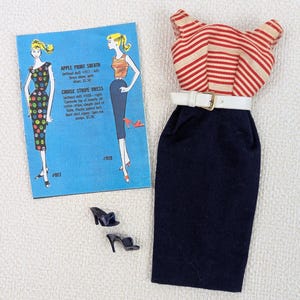 May include: A vintage doll outfit featuring a red and white striped top, a navy blue pencil skirt, and a white belt with a gold buckle. Includes a pair of black high-heeled shoes and a blue card with illustrations and text.