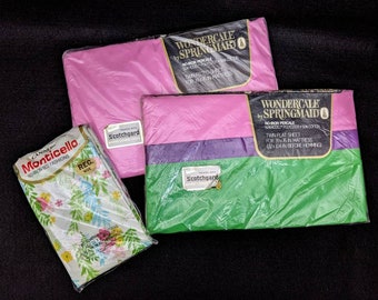 May include: Three packages of twin flat sheets. The top package is pink and says "Wondercale by Springmaid No-Iron Percale Twin Flat Sheet for 39x75 in mattress (92x194 in before hemming)". The middle package is pink, purple, green and says "Wondercale by Springmaid No-Iron Percale Twin Flat Sheet for 39x75 in mattress (92x194 in before hemming)". The bottom package is white with a floral pattern and says "Canno Monticello No-Iron Bed Fashions Reg. Size Treated with Scotchgard".