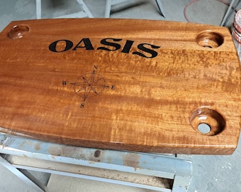 May include: A rectangular wooden serving tray with four circular cutouts for glasses. The tray is stained a warm brown color and features the word "OASIS" and a compass rose design etched into the surface.