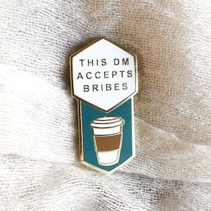 May include: Gold and teal enamel pin with a white hexagon that says "This DM Accepts Bribes". A cartoon coffee cup with a brown lid and brown liquid is inside the hexagon.