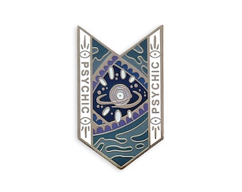 May include: A silver-toned enamel pin in a shield shape, featuring a central design of a planet with rings and an eye. The pin has a blue, white, and purple color scheme, with the word "PSYCHIC" in white on either side.