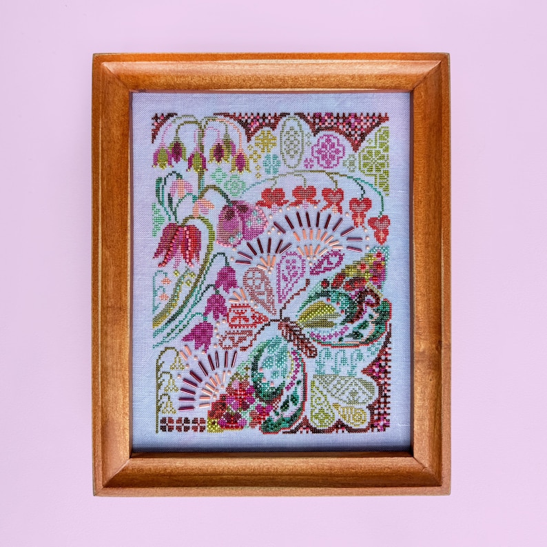 May include: A framed cross-stitch embroidery featuring a butterfly motif composed of intricate floral patterns in shades of red, pink, green, and yellow. The design includes beaded accents and geometric borders on a light blue fabric within a wooden frame.
