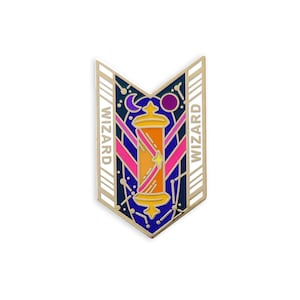May include: A gold-colored enamel pin in a shield shape, featuring a stylized wizard's staff in shades of orange and yellow, with a star, moon, and planets. The word "WIZARD" is printed vertically on both sides of the shield.