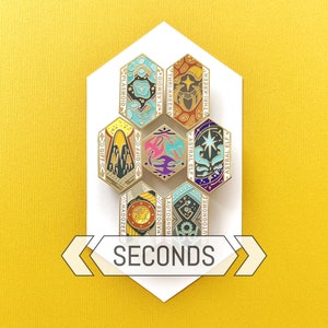 May include: A collection of seven hexagonal enamel pins with gold borders, each featuring unique designs and text. The pins are arranged on a white geometric shape against a yellow background. The word "SECONDS" is displayed below the pins.