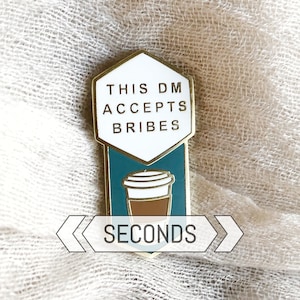 Peut inclure: Épingle en émail dorée avec le texte "THIS DM ACCEPTS BRIBES" au-dessus d'un dessin de tasse à café turquoise et marron. Le mot "SECONDS" est en dessous de la tasse à café. L'épingle est posée sur un fond en tissu neutre.