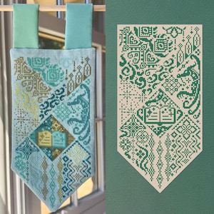 Op de afbeelding: Een verticale wandhanger van stof met ingewikkeld kruissteekborduurwerk in tinten blauwgroen, groen en goud. Het ontwerp bevat geometrische patronen, sterren en een centraal open boek, opgehangen aan een houten roede met twee lichtblauwe lussen.