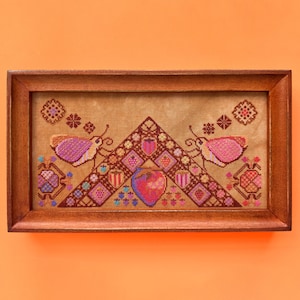 May include: A framed cross-stitch embroidery featuring a geometric design with butterflies and hearts in shades of pink, red, purple, and brown.