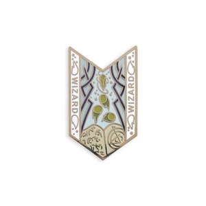 May include: A gold-colored enamel pin with a blue and white design. The pin features a stylized image of a book with a swirling pattern and the word "WIZARD" on either side.