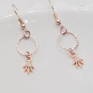 Könnte beinhalten: Ein Paar Ohrringe aus roségold mit einem kleinen, detaillierten Sternchen-Anhänger, der an jedem Kreis hängt.