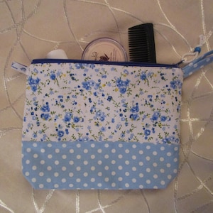 Puede incluir: Una bolsa de cremallera de estampado floral azul y blanco con fondo azul de lunares. La bolsa está abierta y tiene un peine y un pequeño frasco en su interior.