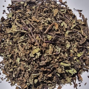 A pile of dried herbs or plant material, possibly tea leaves, on a white surface.