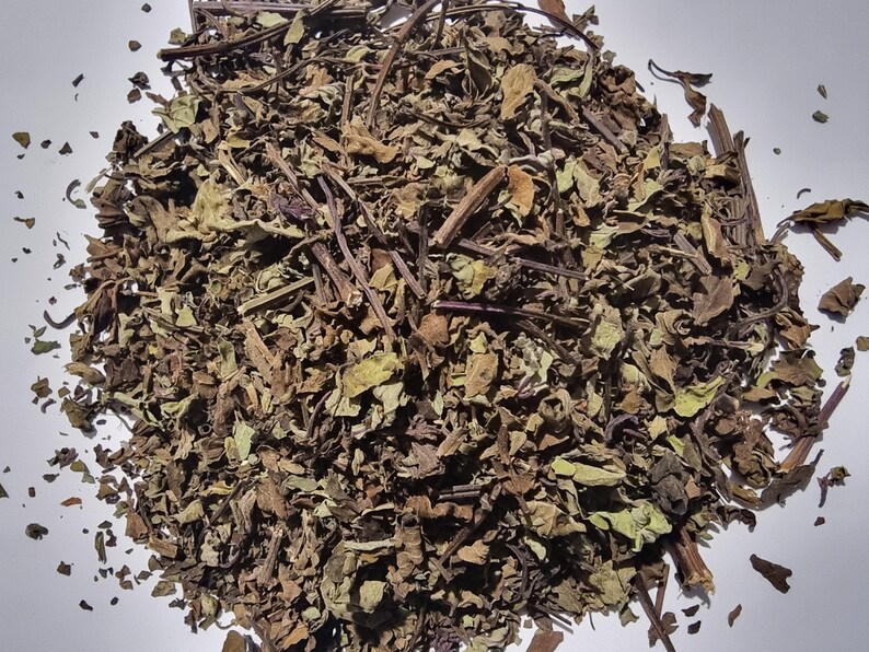 A pile of dried herbs or plant material, possibly tea leaves, on a white surface.