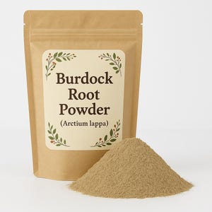 Puede incluir: Una bolsa de papel marrón con una etiqueta que dice "Burdock Root Powder (Arctium lappa)". La bolsa está abierta y se derrama un montón de polvo marrón.