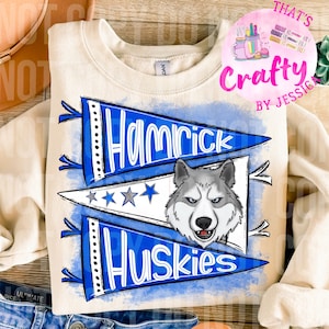 Może przedstawiać: Kremowa bluza z niebiesko-białym wzorem proporczyka. Proporczyki głoszą "Hamrick Huskies" z grafiką psa husky. Projekt zawiera gwiazdy i niebieskie tło w stylu akwareli. Bluza ma okrągły dekolt.