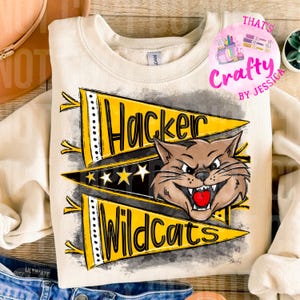 Könnte beinhalten: Cremefarbenes Sweatshirt mit einer Grafik, die einen knurrenden Wildkatzenkopf und die Worte "Hacker Wildcats" auf gelben Wimpeln zeigt. Das Design umfasst Sterne und schwarze Akzente und erzeugt einen kühnen Look im College-Stil.