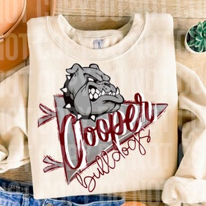 May include: Cream-coloured sweatshirt with a grey bulldog graphic and the maroon text "Cooper Bulldogs". The design is set within a grey and maroon pennant shape. A casual, comfortable apparel item.