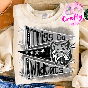May include: Cream-colored sweatshirt with a graphic design featuring the text "Trigg Co Wildcats" on pennant flags, and a gray and white wildcat head. The design includes stars and a distressed background.