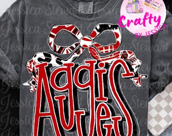 Op de afbeelding: Donkergrijs sweatshirt met het woord "Aggies" in rode en zwarte letters. Een decoratieve strik met rode, witte en zwarte patronen staat erboven. Het shirt heeft een vintage, versleten uitstraling.