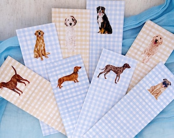 May include: A collection of seven rectangular bookmarks featuring various dog breeds illustrated on light blue or pale yellow gingham backgrounds. Each bookmark displays a single dog, including a golden retriever, dachshund, and pug.