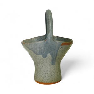 May include: A ceramic basket with a flared rim and a single arched handle. The body features a speckled light green base with a smooth, glossy blue-grey glaze dripping down from the top edge, revealing a terracotta-colored clay rim and base.