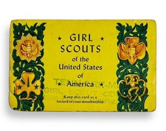 Könnte beinhalten: Eine rechteckige gelbe Mitgliedskarte für die Girl Scouts of the United States of America. Die Karte hat dunkelgrüne florale Ränder und goldfarbene Embleme auf beiden Seiten, mit schwarzem Text, der den Namen der Organisation angibt.